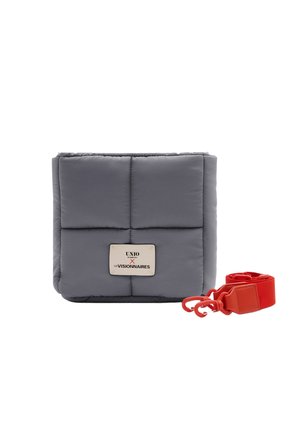 Graue, gesteppte, rechteckige Handtasche mit einem weißen Etikett vorne und einem abnehmbaren, breiten roten Träger mit Haken daneben.