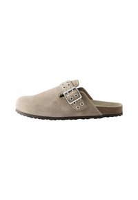 Beige színű, velúr slip-on klumpa széles pánttal, amely ezüst hardware elemekkel és több gromettel díszített; textúrált talp a tapadás érdekében.