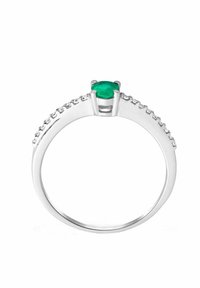 Anello in argento con un centro di smeraldo verde rotondo, circondato da piccole pietre trasparenti lungo la fascia. Finitura liscia e lucida.
