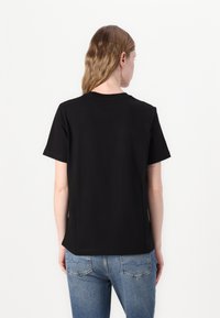Camiseta negra de manga corta hecha de algodón, con cuello redondo y un corte holgado, vista desde atrás con vaqueros azules.