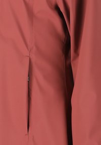 Rød vandtæt jakke med en glat overflade, lynlåslomme i siden og minimale syninger for et strømlinet design. Teksturstof for holdbarhed.