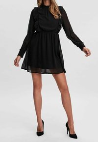 Robe en chiffon noir avec un col montant, des accents à volants, des manches longues et une taille cintrée. Comprend une jupe évasée et une texture transparente.