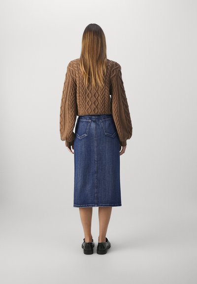 Brun kabelstrikket genser med puffede ermer, kombinert med et denim-midi skjørt med to baklommer og rett snitt. Svarte sko.