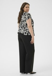 Zwart-wit bloemenpatroon top met korte mouwen, gecombineerd met zwarte wijde broekspijpen en zwarte puntige schoenen, gezien van achteren.