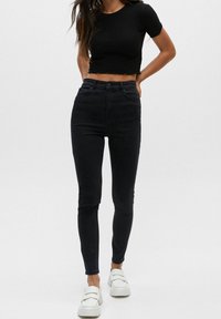 Jean skinny noir taille haute avec une texture lisse, design à cinq poches et détails de couture subtils, associé à un top noir à manches courtes.