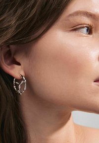 Orecchini in argento con un design astratto e tortuoso a forma circolare. La texture liscia e la finitura riflettente completano l'orecchio.