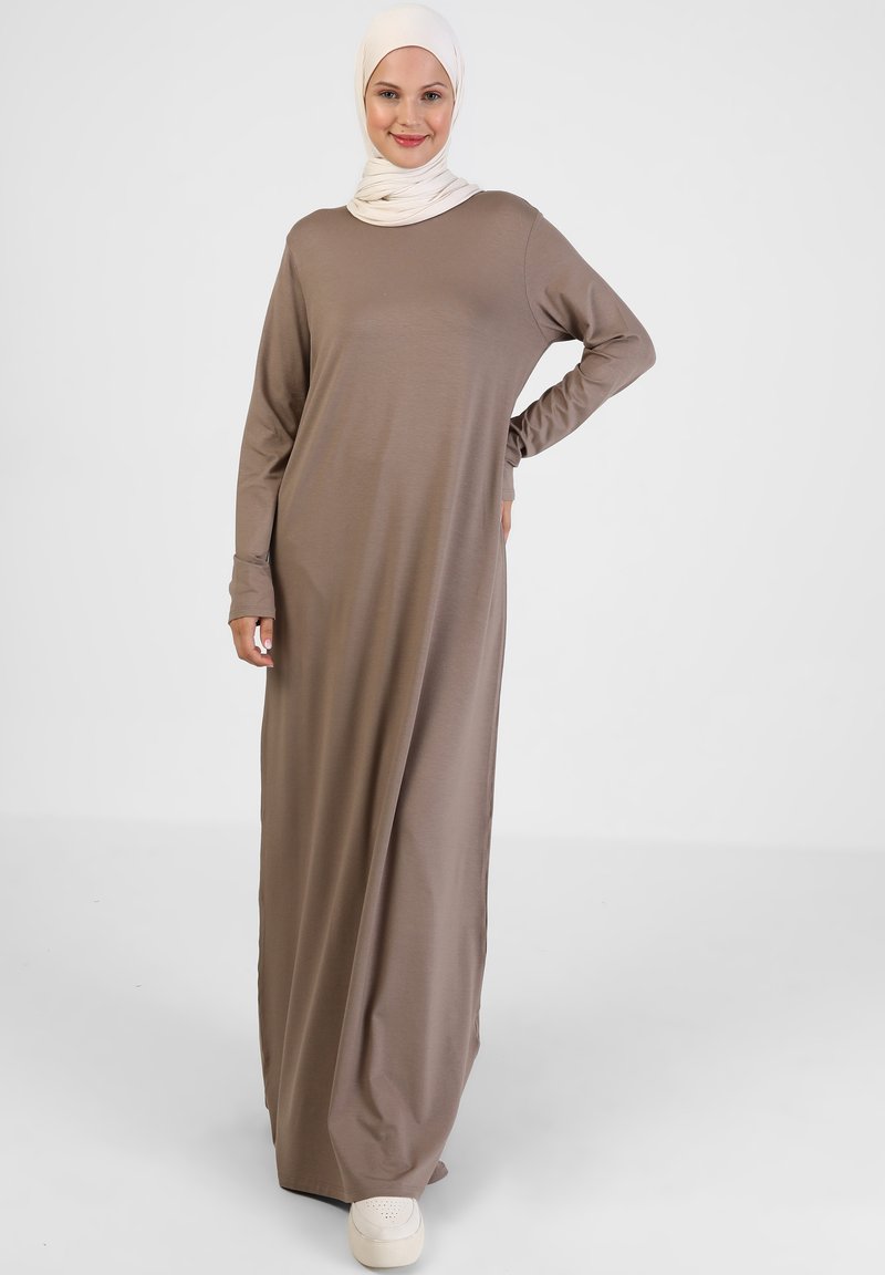 Langes, braunes Kleid aus weichem Stoff mit langen Ärmeln, einem runden Ausschnitt und lockerer Passform, kombiniert mit hellen Schuhen.