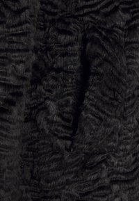 Tissu en fausse fourrure noire avec une surface douce et texturée présentant des crêtes et des motifs variés, adapté aux vêtements ou à l'ameublement.