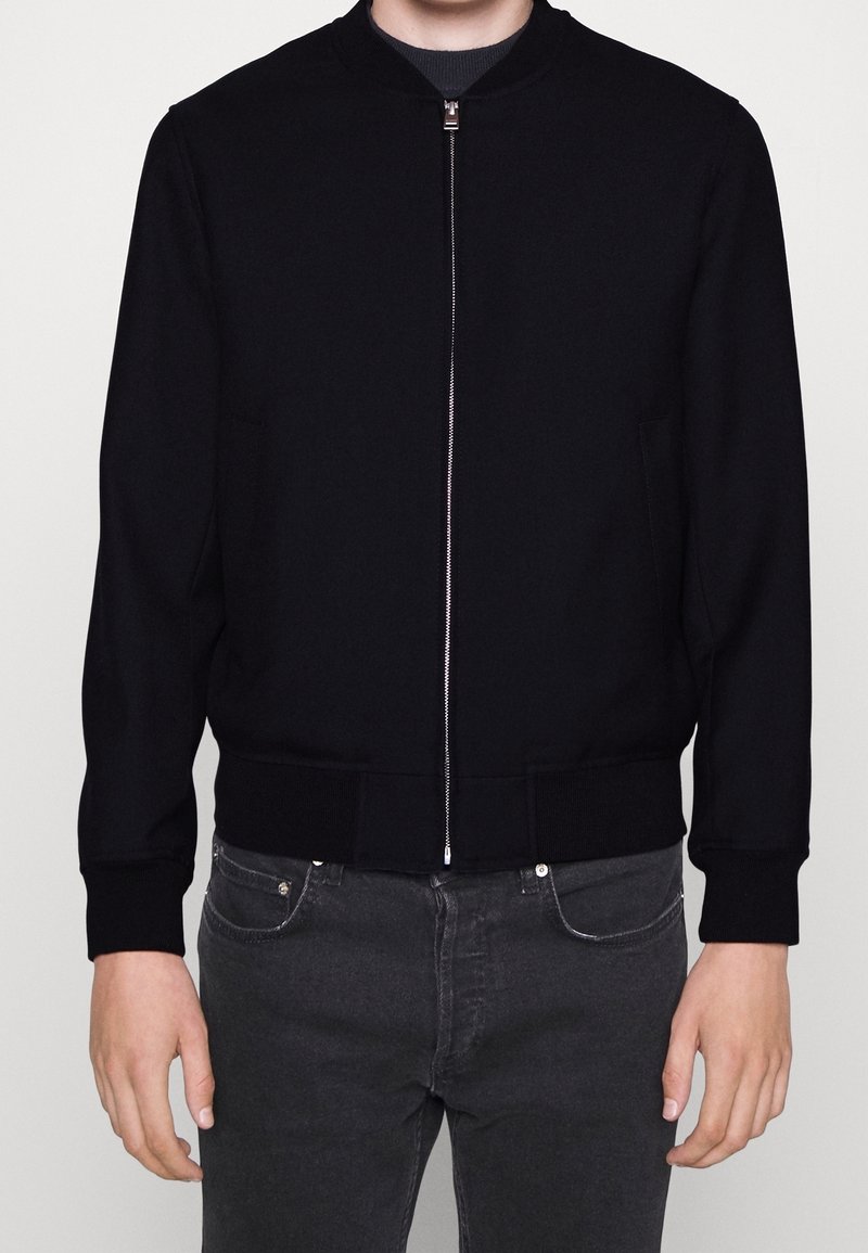 Giubbotto bomber nero con zip frontale, polsini e orlo a costine, realizzato in un tessuto liscio. Include tasche laterali e collo rotondo.