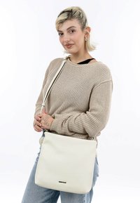 Bílá kožená kabelka s texturovaným povrchem, s dlouhým nastavitelným popruhem a jemným logem značky na přední straně.