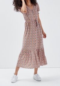 Vestido midi floral en rosa con mangas cortas, escote en V y dobladillo con volantes. La tela presenta pequeños patrones de flores multicolores. Se lleva con zapatillas blancas.