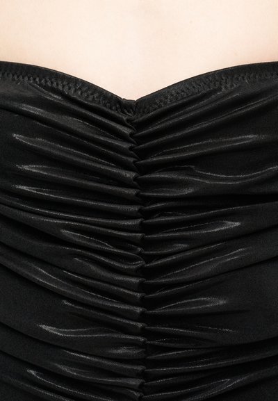 Κοντινό πλάνο μαύρου ραβδώματος υφάσματος που συγκεντρώνεται στο κέντρο πάνω σε ανοιχτόχρωμο δέρμα, δείχνοντας λεπτομέρειες υφής και ραφών.