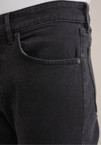 Černé džíny z denimu s hladkou Texturou, které mají klasický design s pěti kapsami a jemné detaily šití. Knoflíky a zipy jsou černé.