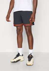 Sorte sportsbukser med orange striber, lavet af et struktureret stof. Båret med beige og sorte sneakers samt hvide ankelstrømper.