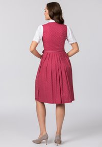 Weinrotes Kleid mit Falten, gemusterter Stoff und tailliertem Oberteil. Darunter befindet sich eine weiße Bluse und dazu graue High Heels.