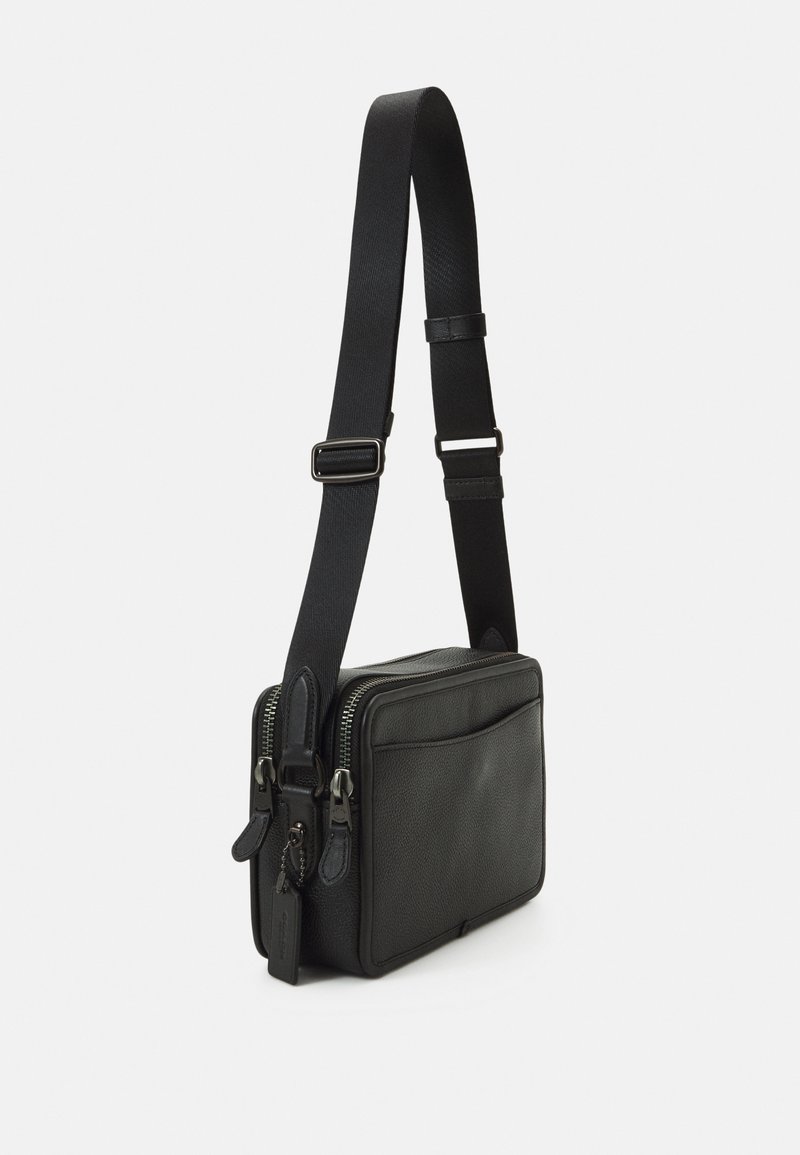 Sac en cuir noir à bandoulière avec deux compartiments zippés, une sangle en tissu réglable et une texture lisse. L'avant comporte une poche plate.