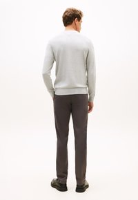 Szürke hosszú ujjú, V-nyakú pulóver sötétszürke nadrággal párosítva. Fekete cipők vastag talppal egészítik ki a szettet.