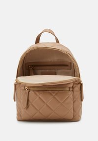 Quilted beige backpack with a top handle, gold zippers, and multiple compartments. Smooth texture and structured shape.