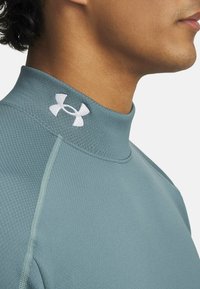 Top atlético azul claro hecho de una tela suave y elástica, con un cuello alto y un logo blanco bordado en el escote.