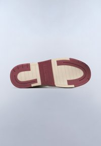 Sulan på en sko med en vinröd gummidel och krämfärgade strukturerade mönster. Har en logo präglad nära hälen. Platt, bred design.