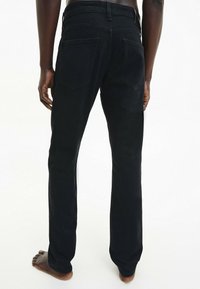 Jeans in denim nero con taglio dritto, dotati di due tasche posteriori e una vita pulita. Il tessuto ha una texture liscia e un minimalismo nei dettagli.