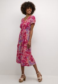 Robe maxi rose vibrante avec un motif paisley en bleu et turquoise, manches courtes, décolleté en V et taille cintrée.