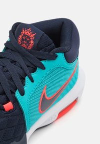Blauwe en groene sneaker met een gestructureerde bovenkant, rode accenten en een opvallend grijs Nike-logo. Voorzien van een gewatteerde kraag en veters.