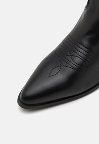 Black leather ankle boot with a pointed toe, featuring embossed horizontal stitching and decorative patterns on the upper.
