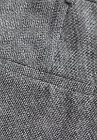 Grijze stof met een gestructureerd weefsel, met een close-up van een zakdetail. Het oppervlak heeft een subtiel patroon en een gelijkmatige kleurverdeling.