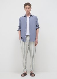 Chemise boutonnée bleu clair, t-shirt blanc en dessous, pantalon rayé crème et bleu, sandales marron. Design simple et décontracté.