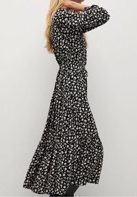 Schwarzes Blumenkleid mit langen Ärmeln, das eine taillierte Taille und einen gestuften Rock aufweist, geschmückt mit weißen Blumenmustern.