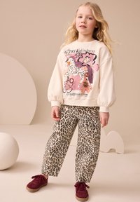 Bluză crem deschis cu imprimeu colorat cu cal și text, asortată cu pantaloni largi cu imprimeu leopard și pantofi burgundi.