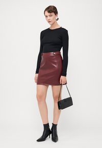 Black long-sleeve top, burgundy faux leather mini skirt with side button detail, black ankle boots, and a small black handbag with a chain.