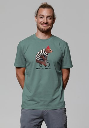 Green cotton t-shirt featuring a bear in a striped outfit and red hat on a unicycle, with text "Pour de Frans" below the graphic.