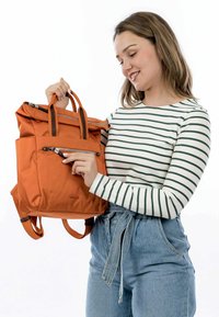 Zaino in tessuto arancione con doppi manici superiori, spallacci regolabili e una tasca anteriore con zip. Presenta un design a ribalta e hardware in argento.