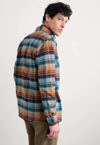Camicia in flanella a quadri con colori blu, arancione e verde; presenta un colletto classico, polsini con bottone e una vestibilità rilassata. Tessuto morbido e texturizzato.