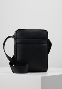 Borsa a tracolla nera in pelle con finitura texture, forma rettangolare, chiusura con zip superiore e tracolla regolabile. Design minimalista con tasca frontale.