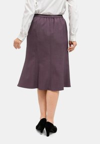 Lila A-Linien-Rock mit elastischem Bund, aus strukturiertem Stoff gefertigt. Der Saum reicht unter das Knie und wird mit schwarzen High Heels kombiniert.