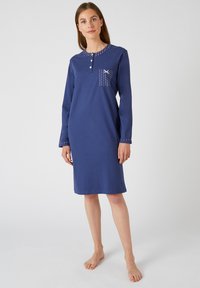 Camicia da notte in cotone blu navy con maniche lunghe, scollatura con bottoni e tasca decorata con piccoli punti bianchi. Texture liscia in tutto il capo.
