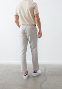Light beige short-sleeve shirt paired with gray pants. The pants have a flat front, straight cut, and back pocket. White sneakers feature navy accents.