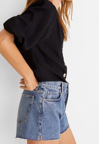 Černý pruhovaný top s krátkými rukávy a detaily na knoflík, doplněný o džíny s vysokým pasem a roztrhanými okraji v světle modré barvě.