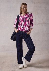 Blusa multicolore rosa e bianca con un motivo a V, maniche arrotolate; jeans a gamba larga blu scuro; sneakers bianche; borsa a tracolla nera.