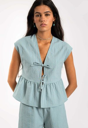 Top corto de cuadro vichy azul claro con mangas cortas tipo capaza, un escote en V profundo y detalle de lazo en la parte delantera. Diseño peplum con tejido texturizado.
