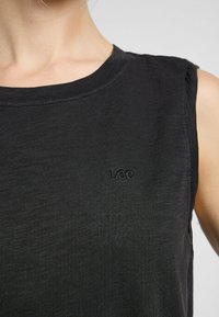 Sort ærmeløs top lavet af tekstureret stof. Har en rund halsudskæring og et diskret broderet logo på brystet.