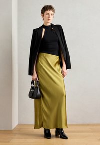 Black sleeveless top and a high-waisted olive green satin maxi skirt, paired with a black handbag and heeled black boots.