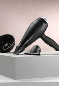 Musta BaByliss-hiustenkuivain, jossa diffuusori, keskittävä suutin ja muotoilusuutin, lepää harmaalla pinnalla beigen taustan edessä.