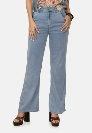 Jeans de pierna ancha color azul claro con cintura alta, presentan bolsillos delanteros y cierre de botón. Combinados con sandalias de tacón marrones.