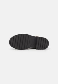Suela de zapato de goma negra con surcos verticales para tracción, presenta un diseño plano y un logotipo de marca en relieve en el centro.