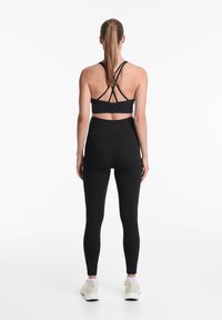 Fekete sportos melltartó, hátul keresztpántokkal, magas derékú fekete leggingsszel és világos színű sportcipővel párosítva.