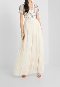 Langes Elfenbein-Tüllkleid mit V-Ausschnitt, bestickten Blumenakzenten und kurzen, flatternden Ärmeln. Der fließende Rock sorgt für Textur und Bewegung.